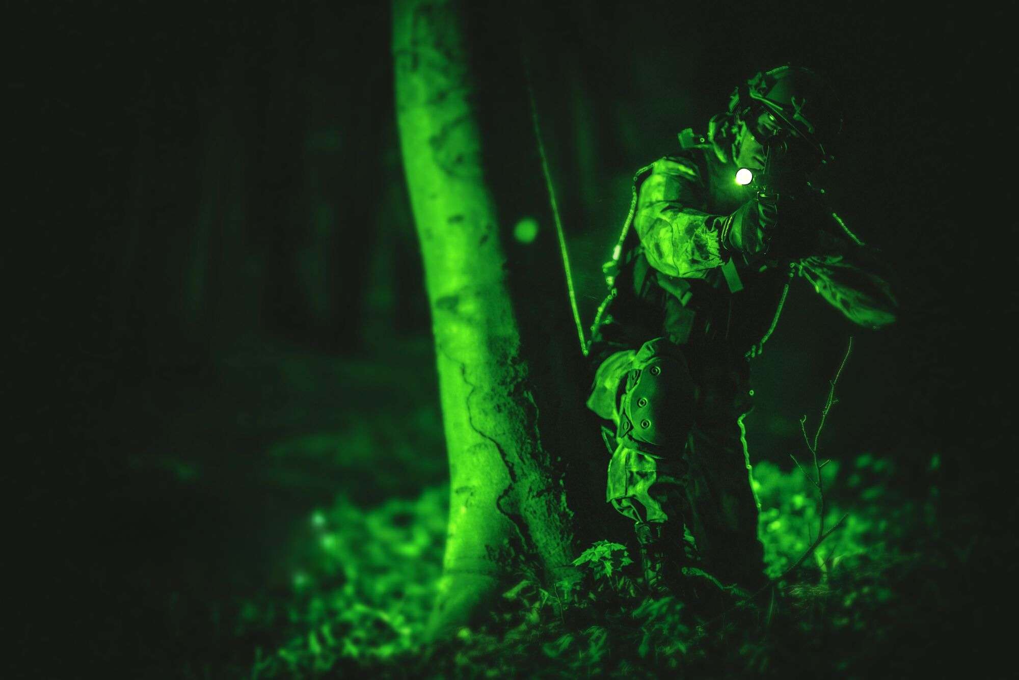 night vision soldier crouched behind tree