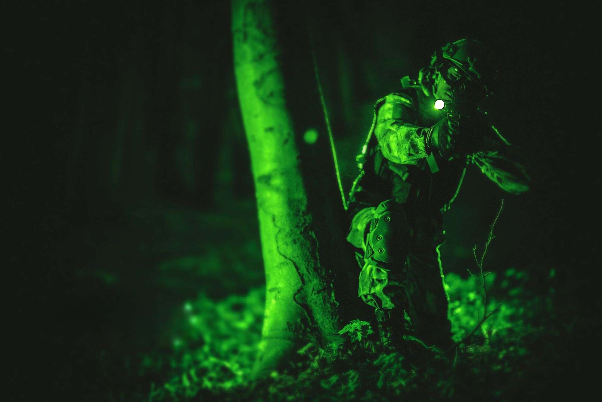 night vision soldier crouched behind tree low light